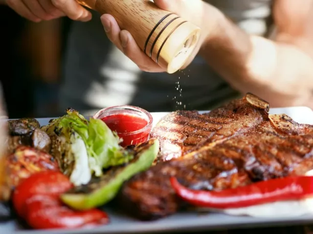 Man cracking black pepper on his steak and grilled veggies on the keto diet