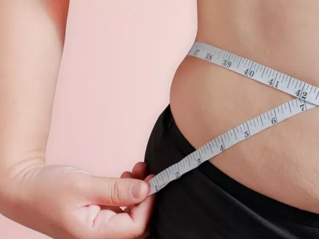 Woman measuring her torso with a tape measure, upset she's in a weight loss plateau