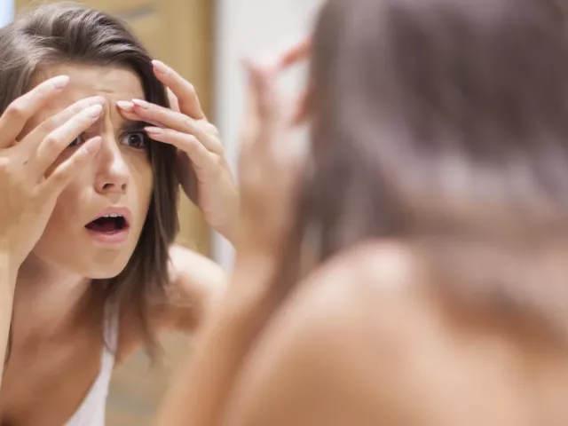 Woman examining forehead for acne
